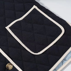 Close-up of a quilted black jacket with a button and white trim.