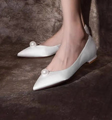 White pointed-toe shoes with pearl accents on a dark brown fur background