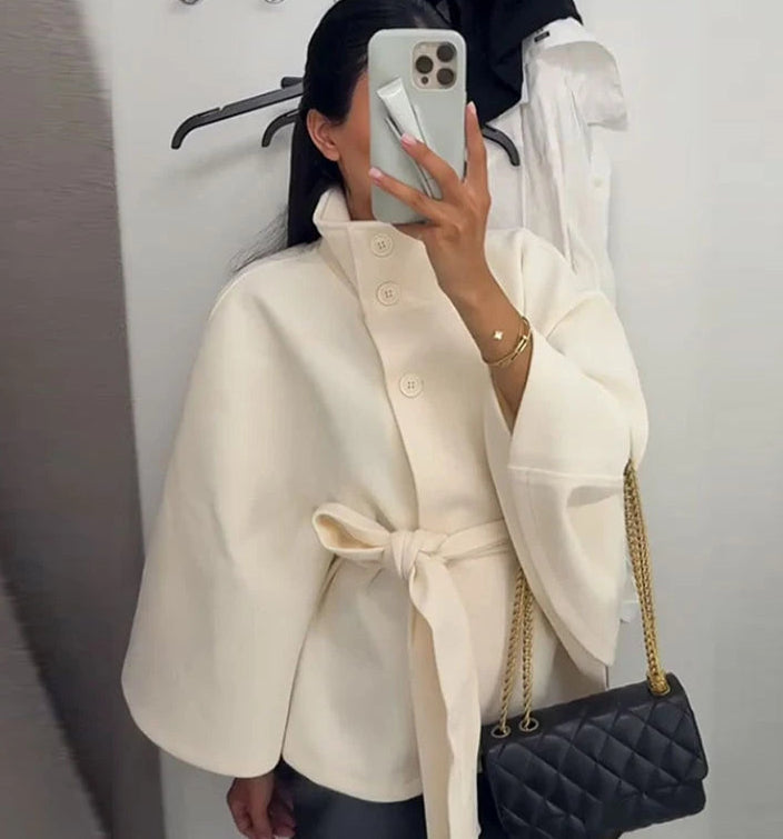 Person wearing a cream coat holding a black quilted handbag.