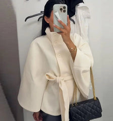 Person wearing a cream coat holding a black quilted handbag.