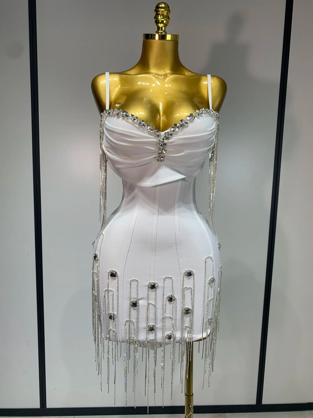 White dress with embellishments on a gold mannequin against a plain background