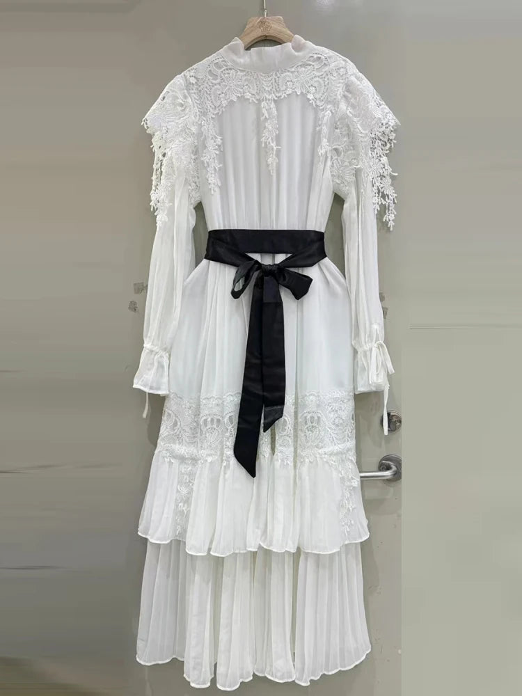 White lace dress with a black belt on a hanger against a neutral background