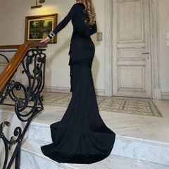 Woman in a black evening gown standing on a staircase in an elegant interior setting.