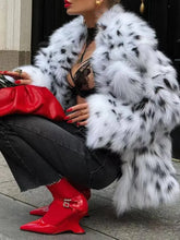 Person wearing a white fur coat with black spots, red boots, and black pants sitting on a step.