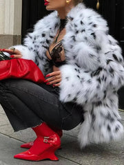 Person wearing a white fur coat with black spots, red boots, and black pants sitting on a step.