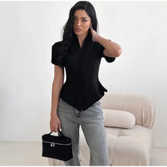 Woman wearing a black shirt and gray jeans holding a black handbag in a minimalistic room.
