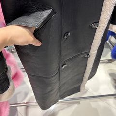 Close-up of a black leather jacket with buttons, held by a hand.