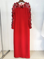 Red dress with floral embellishments on a hanger against a white wall.