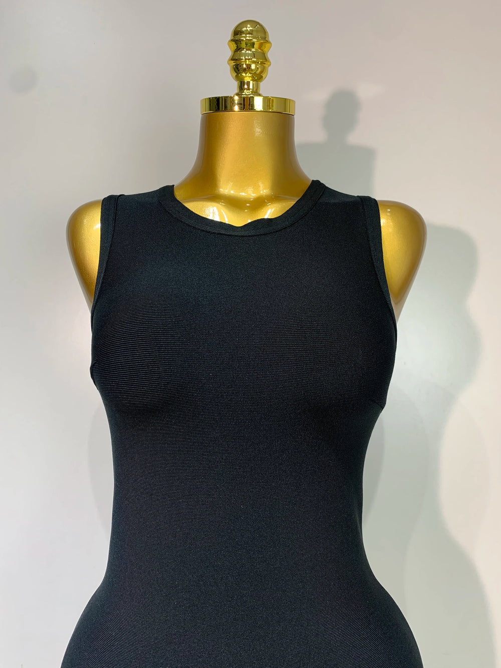 Black sleeveless top on a gold mannequin against a white background