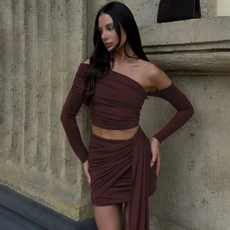 Woman wearing a brown one-shoulder dress against a stone wall.