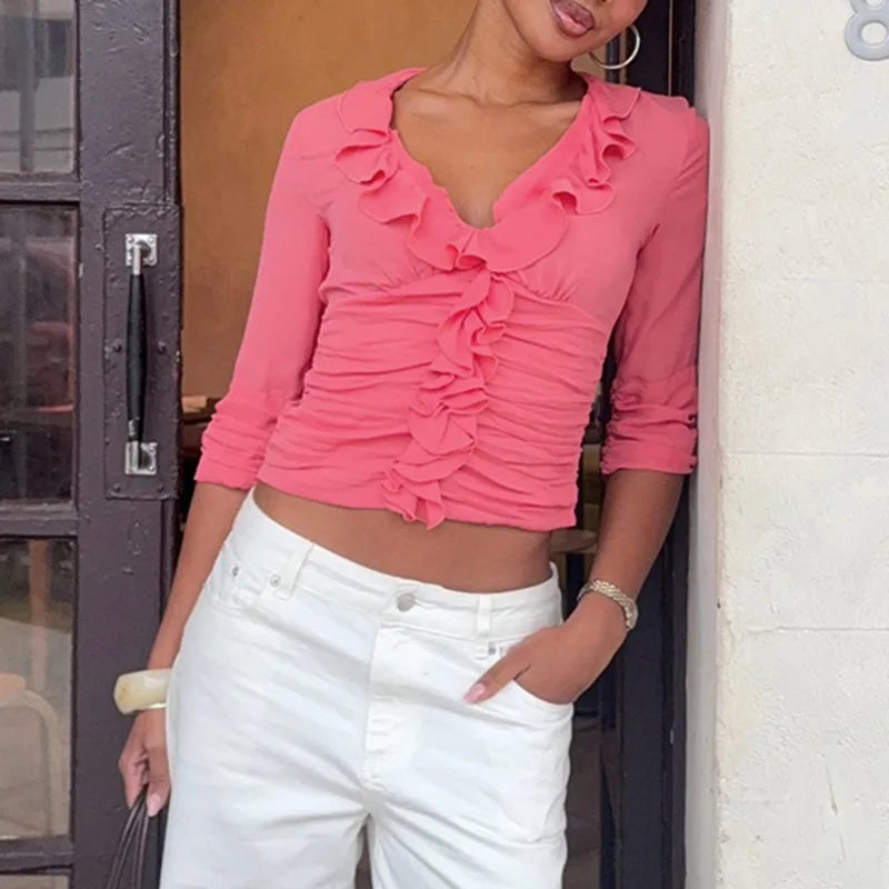 Model wearing a pink ruffle V-neck cropped top with white pants.