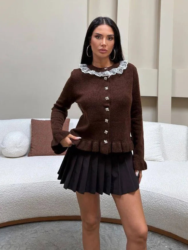Woman wearing a brown cardigan with lace collar and black pleated skirt in a living room setting.