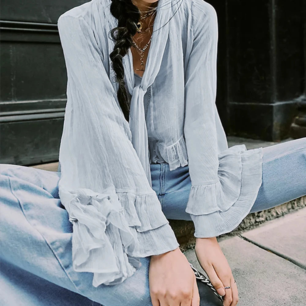 Person wearing a light blue blouse with ruffled sleeves sitting on a bench.
