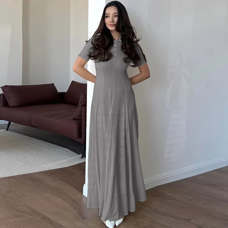 Woman in a long gray dress standing in a minimalistic room with a sofa and rug.