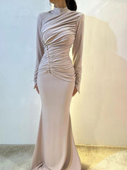 Woman wearing a long, light-colored dress with a fitted silhouette against a neutral background.