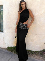Woman in a black one-shoulder dress with a sequined waistband standing against a light-colored wall.