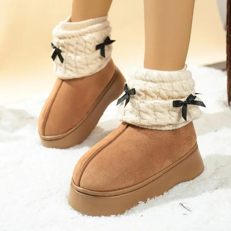 Tan snow boots with white cuffs and black bows on a snowy background