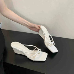 White wedge sandals on a black surface with a neutral background