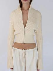Person wearing a beige ribbed zip-up cardigan over a white top and pants on a light gray background