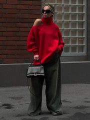 Person wearing a red sweater and dark pants, holding a black handbag against a brick wall.