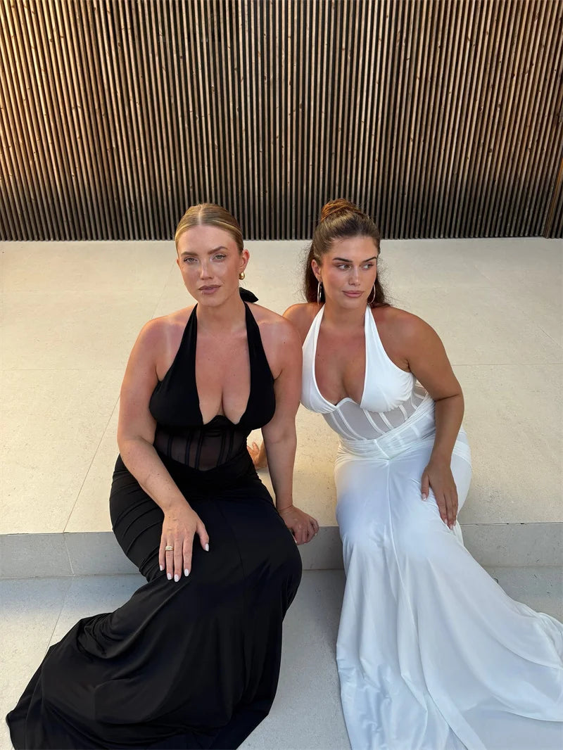 Two women in elegant dresses sitting on a bench with a modern architectural background.