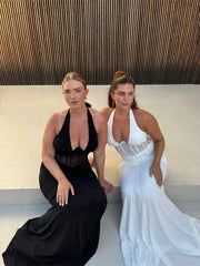 Two women in elegant dresses sitting on a bench with a modern architectural background.