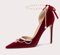 Red high-heeled shoe with gold chain and pearl decorations on a light gray background