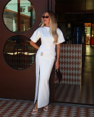 Woman in a white outfit standing in front of a patterned wall.
