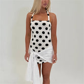 Woman wearing a black and white polka dot swimsuit cover-up on a plain background