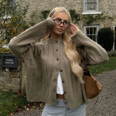 Woman wearing a beige cardigan in front of a stone building