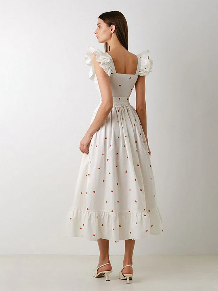 Woman wearing a white dress with floral sleeves against a plain background