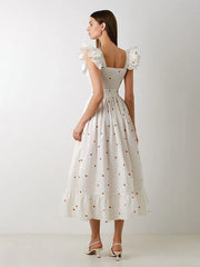 Woman wearing a white dress with floral sleeves against a plain background