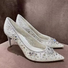 White high-heeled shoes with crystal embellishments on a brown surface