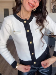 Woman wearing a white and black cardigan with gold buttons in an indoor setting.