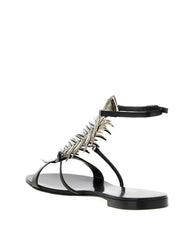Side view of a black flat sandal with a silver rhinestone fishbone embellishment and ankle strap