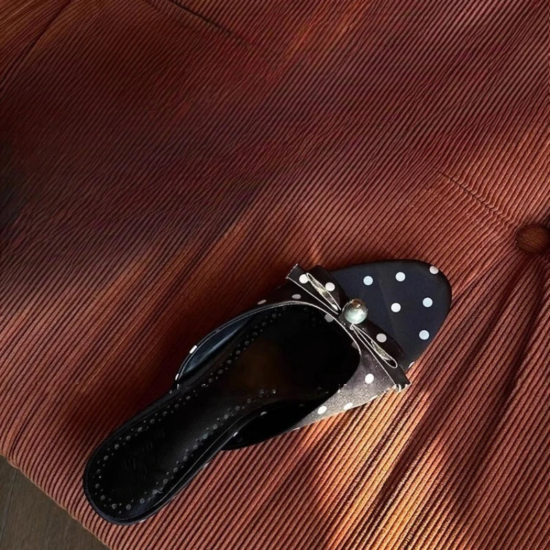 Black flat shoes with white polka dots on a brown textured surface