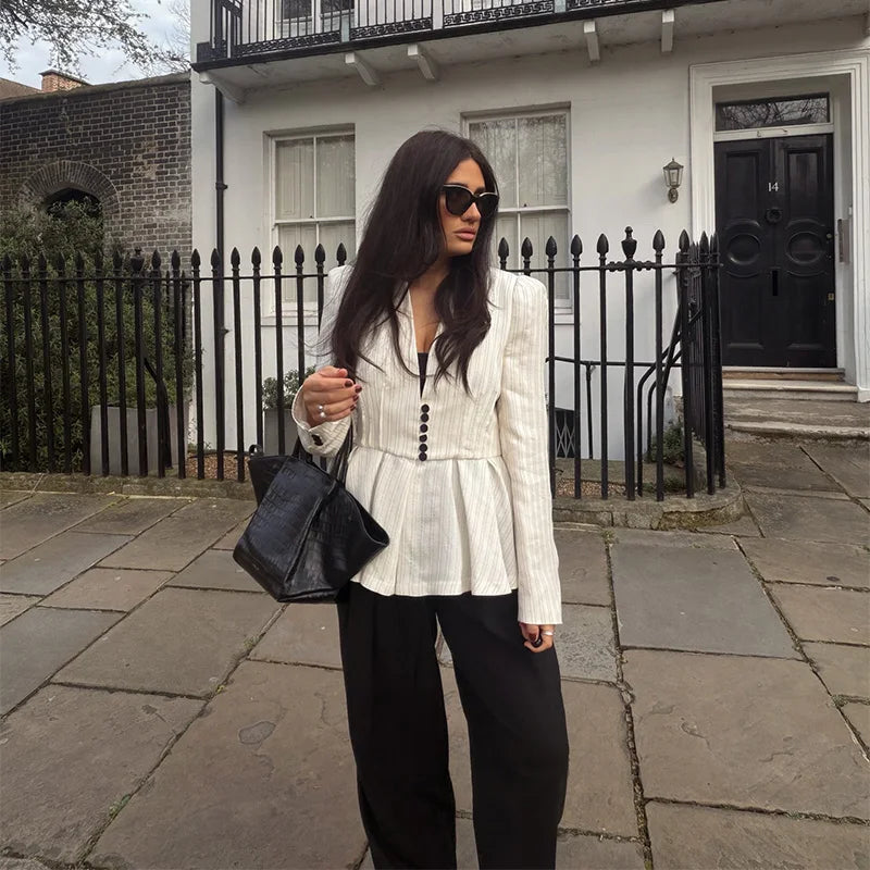 Woman in a white peplum top and black pants standing on a street.
