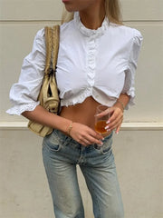 Person wearing a white blouse with ruffled details and blue jeans, holding a drink.