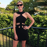 Woman in a black dress with cut-out design standing outdoors with greenery in the background