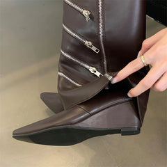Brown leather boot with zippers being adjusted by a hand on a neutral background