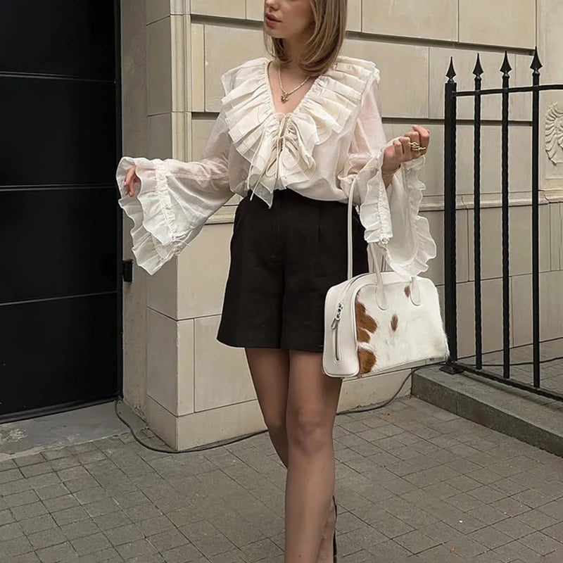 Woman wearing a white blouse with ruffles and black shorts, holding a cow print handbag.