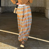 Person wearing plaid pants and a mustard jacket on a concrete floor.
