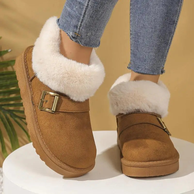 Brown suede boots with white fur trim and gold buckles worn with blue jeans on a beige background.