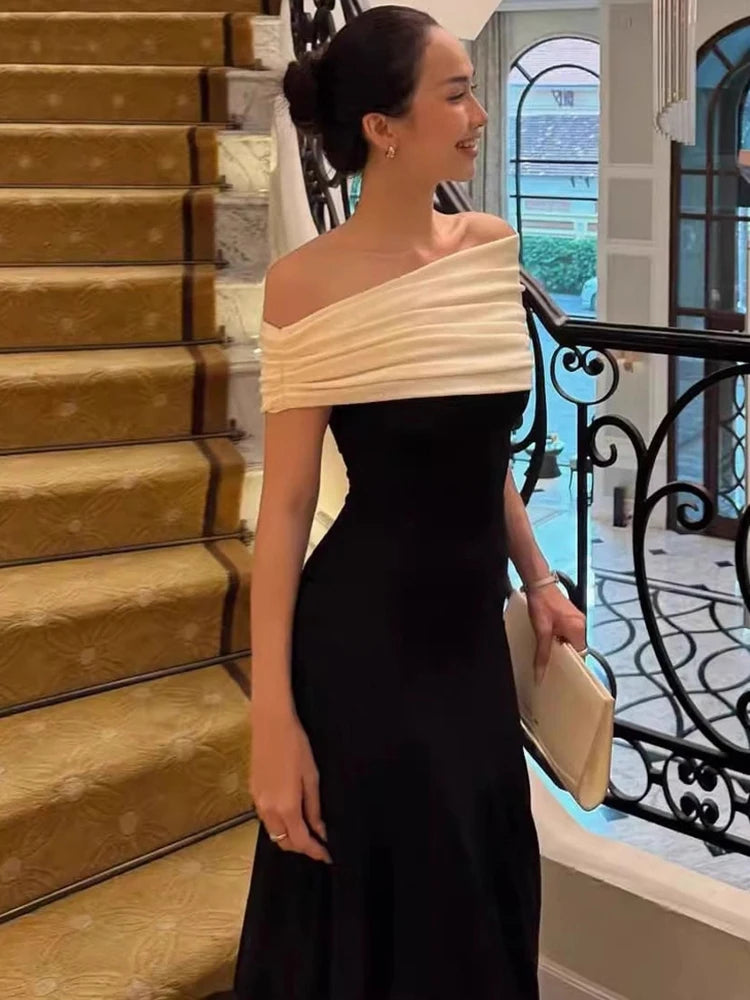 Woman in a black and beige off-shoulder dress standing in an elegant interior setting.