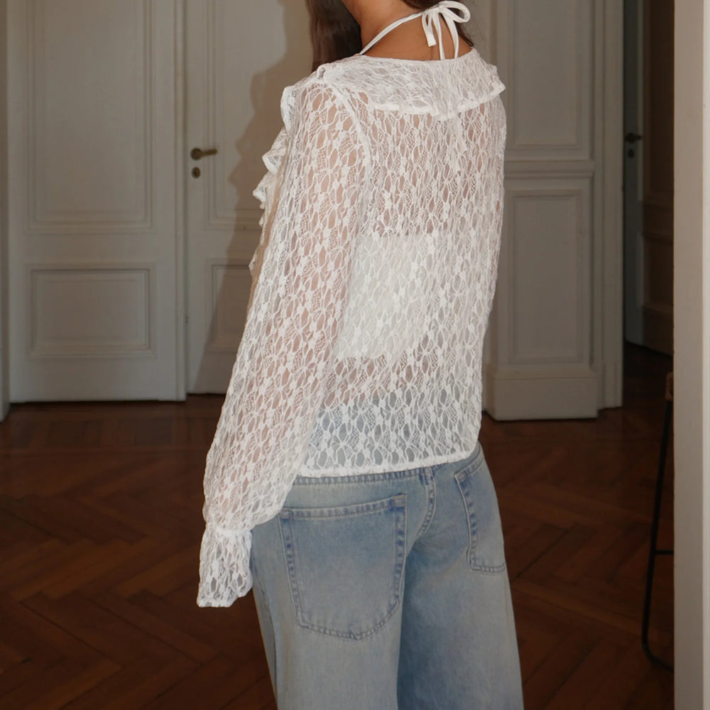 Person wearing a sheer white lace top and light blue jeans indoors.