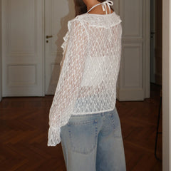 Person wearing a sheer white lace top and light blue jeans indoors.