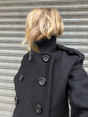 Person wearing a dark coat with button details against a metallic background