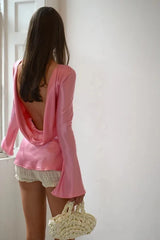 Woman wearing a pink open-back top and white shorts, standing in a room with a white door.