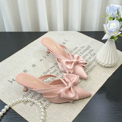 Pink high-heeled shoes with bows on a surface with text and a vase of flowers.