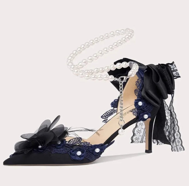 Black high-heeled shoe with floral design and pearl details on a light gray background